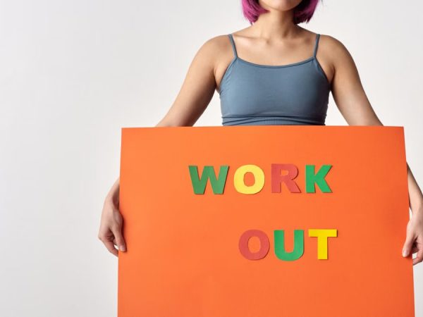 Woman with short hair holding a vibrant 'Work Out' sign on a white background.